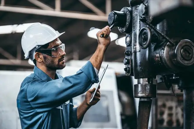 Technicians in hard hat inspect machinery while recording findings on a tablet.